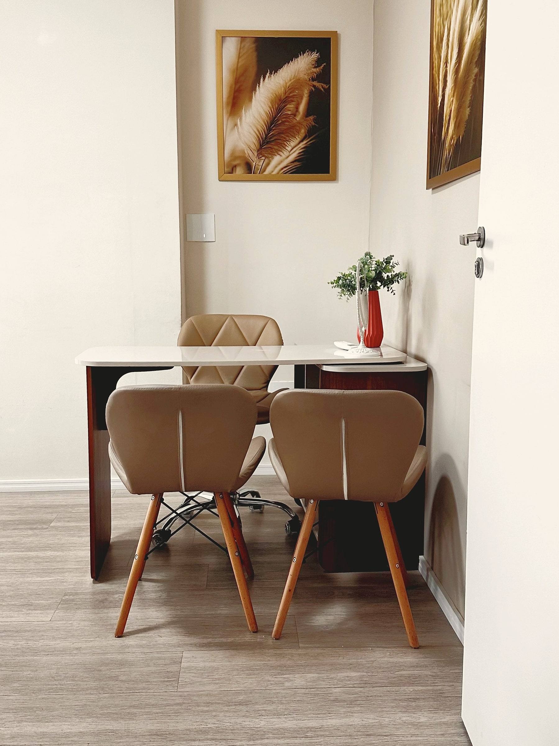 Sala de atendimento com mesa clara, cadeiras bege e quadros de capim-dos-pampas